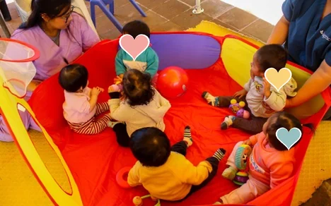 Cuidadoras jugando con bebés dentro de una piscina de juegos roja