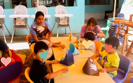 Niñas y niños haciendo manualidades en la mesa con sus maestras