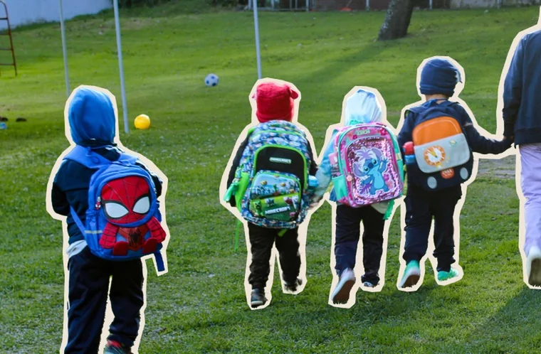 Niñas y niños caminando de la mano de su cuidadora hacia el aula, con sus mochilas
