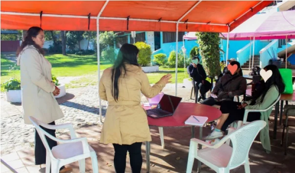 Trabajadora social dando una charla a familias bajo una carpa en el jardín